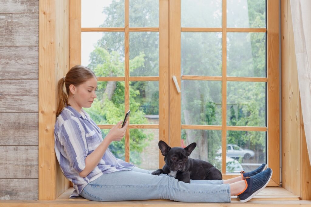 窓際でスマホを触る女性と犬