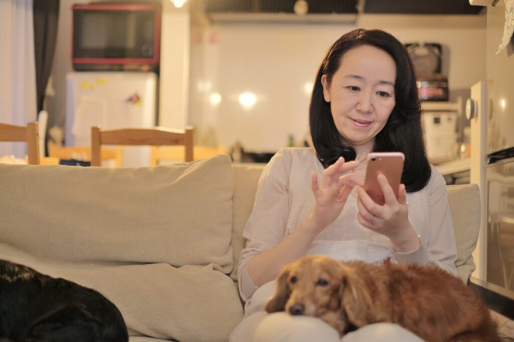 膝に犬を乗せてスマホを触る女性